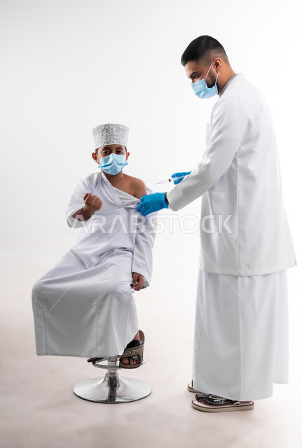 The availability of vaccination against the Corona virus for children, a portrait of a doctor wearing the coat and medical gloves, gives the dose of the Kofid vaccine - 19 to an Arab Gulf Arab child, adhering to safety procedures, following the laws of the Ministry of Health, body with full length, white background