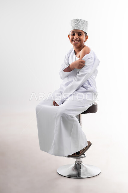 الالتزام بإجراءات السلامة، اتاحة تلقي التطعيم ضد فايروس كورونا للاطفال، بورتريه لطفل عربي خليجي عماني يرتدي الدشداشة والكمه يقوم بتحضير نفسه لتلقي لقاح كوفيد-19، اتباع قوانين وزارة الصحة، خلفية بيضاء