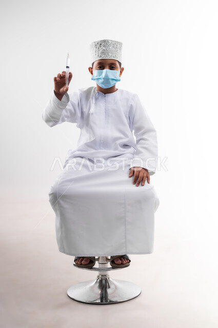 تحديد مهنة المستقبل منذ الصغر، طموحات الأطفال في العمل بالمجال الطبي، بورتريه لطفل عربي خليجي عماني مبتسم يرتدي الدشداشة والكمه  ويحمل بيده إبرة، مفهوم الطب و الرعاية الصحية الأولية ، مهنة إنسانية واجتماعية، الجسم بالطول الكامل، خلفية بيضاء
