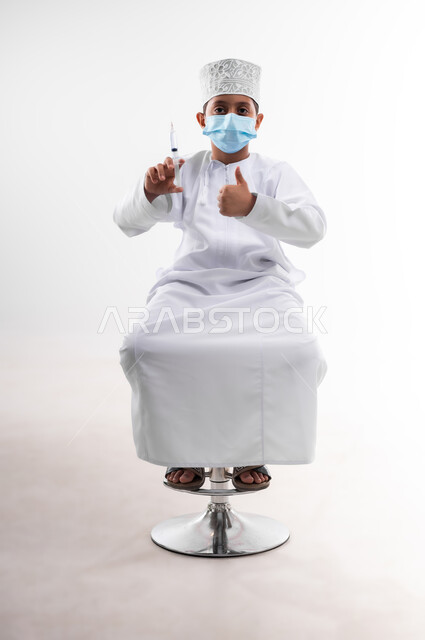 تحديد مهنة المستقبل منذ الصغر، طموحات الأطفال في العمل بالمجال الطبي، بورتريه لطفل عربي خليجي عماني مبتسم يرتدي الدشداشة   ويحمل بيده إبرة، مفهوم الطب و الرعاية الصحية الأولية، اتخاذ الإجراءات الاحترازية للوقاية من فايروس كورونا، خلفية بيضاء