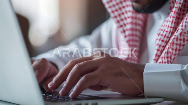 Integrating work with technology, working in the economic field, accomplishing the required tasks, Saudi office professions and jobs, managing and organizing company affairs through technical devices, close-up image of a Saudi Arabian Gulf man wearing traditional dress and a shemagh working on a laptop