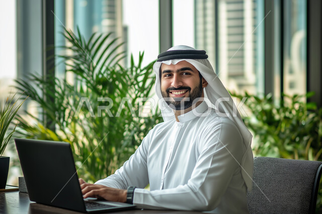 Business Administration and Organization, Image of a smiling Saudi Arabian Gulf man working on a computer inside the office, working to achieve goals and strategies, office administrative professions and jobs, using modern and advanced technological devices