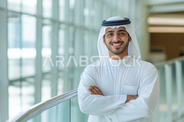 مفهوم الأناقة والإهتمام بالمظهر الخارجي، رجل أعمال عربي خليجي سعودي مبتسم يرتدي الثوب التقليدي ينظر الى الكاميرا يقف باستقامة وايدي متقاطعة، مهن ووظائف ادارية سعودية، توضيح مهام العمل واستراتيجيات الشركة