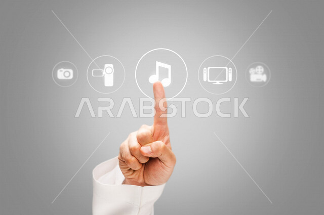 صورة مقربة ليد رجل عربي خليجي سعودي، اختيار زر تشغيل الموسيقى، اشارة وبصمة، مجموعة من الايقونات الخاصة بالانشطة المختلفة، السحابة الالكترونية، ازرار تشغيل، تقنيات مختلفة، رموز رقمية الكترونية