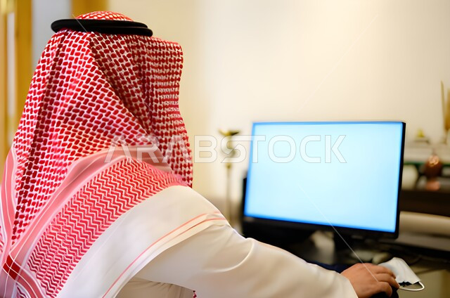 عقد إجتماع عمل عبر الإنترنت، التسويق الإلكتروني، تصفح الإنترنت ، صورة مقربة من الخلف لرجل عربي خليجي سعودي يستخدم جهاز الحاسوب المحمول لإنجاز المهام ، جلسة عمل ، إنجاز المشاريع والمهام، مهن وأعمال تجارية، متابعة ومناقشة العمل