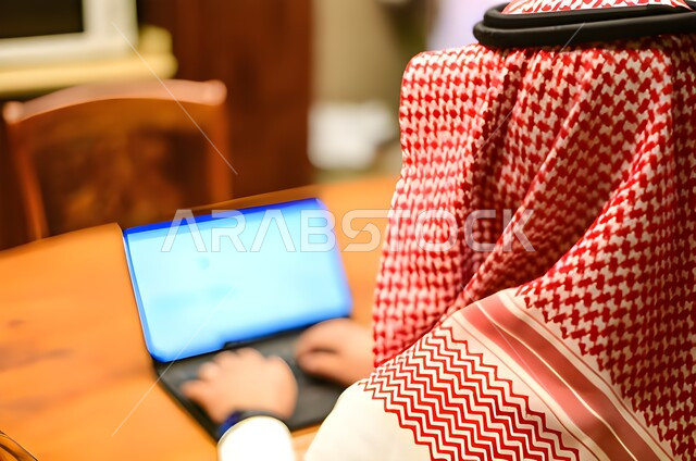 عقد إجتماع عمل عبر الإنترنت، التسويق الإلكتروني، تصفح الإنترنت ، صورة مقربة من الخلف لرجل عربي خليجي سعودي يستخدم جهاز الحاسوب المحمول لإنجاز المهام ، جلسة عمل ، إنجاز المشاريع والمهام، مهن وأعمال تجارية، متابعة ومناقشة العمل