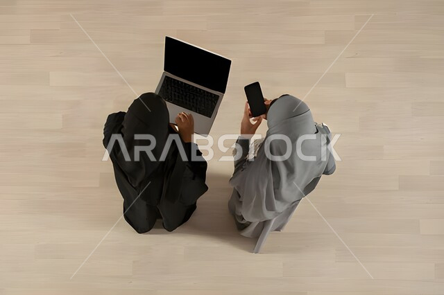 التعاون والتفاهم بين الفريق, تبادل الخبرات والاتفاقيات الناجحة,  بورتريه علوي عامودي لسيدتين عربيتين خليجيتين سعوديتين في اجتماع عمل, ارتداء اللباس السعودي التقليدي, بيئة العمل المريحة في الشركة السعودية, دمج التكنولوجيا في الحياة  العملية, خلفية بيج