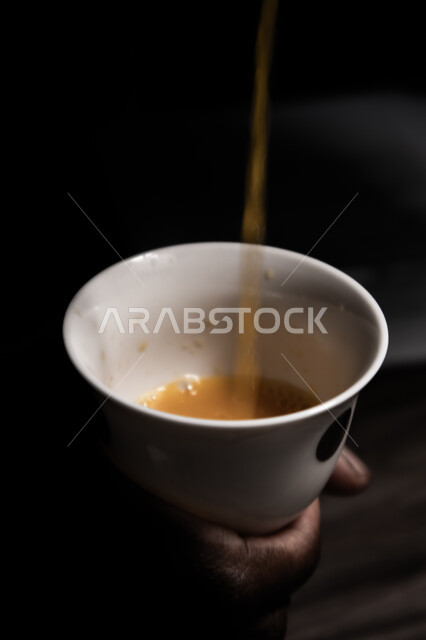 المنتجات والمحاصيل المحلية الوطنية، كرم الاستقبال وحسن الضيافة في المملكة، الاستمتاع بالمشروبات الساخنة، صورة مقربة ليد رجل عربي سعودي يقوم بصب فنجان من القهوة العربية السعودية