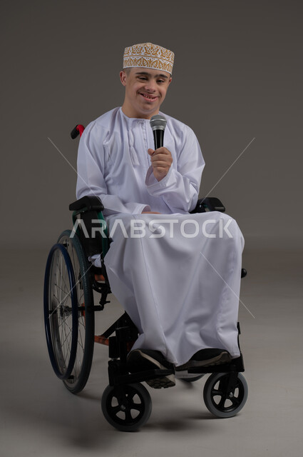 مفهوم الانسجام بالغناء، ذوي الإحتياجات الخاصة والهمم, بورتريه لشاب عربي خليجي عماني يرتدي الكمه والدشداشة يجلس على كرسي متحرك ويحمل بيده مايكروفون، خلفية رمادي