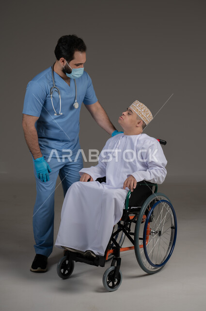 طبيب يشرف على علاج شخص من ذوي الإحتياجات الخاصة والهمم, مفهوم تقديم المساعدة والدعم والعلاج, بورتريه لشاب عربي خليجي عماني يرتدي الكمه والدشداشة يجلس على كرسي متحرك, خلفية رمادي
