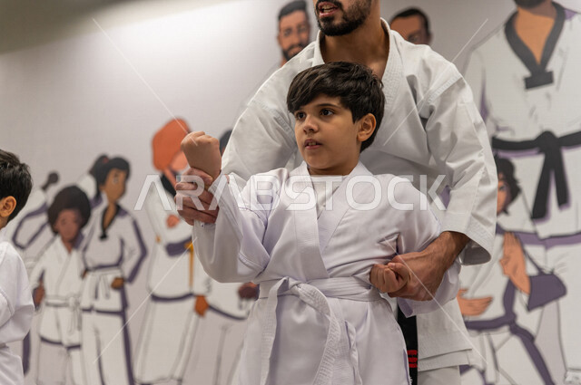 فتى عربي خليجي سعودي يقوم بالتدرب على الحركات القتالية بمساعدة مدرب خليجي سعودي خاص برياضة الكارتيه اليابانية ، التدرب على فنون الدفاع عن النفس ، رياضة دفاعية تتميز بالأخلاق العالية للاعبين