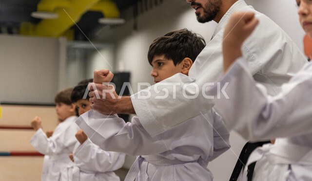 A picture of a Saudi Gulf Arab boy training in combat movements with the help of a Saudi Gulf coach specializing in Japanese karate, training in martial arts, a defensive sport characterized by high morals for players