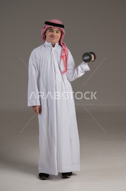 مفهوم الرياضة والصحة البدنية, ممارسة التمارين الرياضية, ذوي الإحتياجات الخاصة والهمم, بورتريه لشاب عربي خليجي سعودي يرتدي الثوب والشماغ صورة الجسم بالطول الكامل, خلفية رمادي