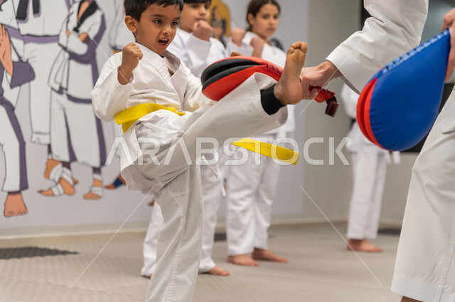 فتى عربي خليجي سعودي يقوم بالتدرب على الحركات القتالية  بمساعدة مدرب خليجي سعودي خاص برياضة الكارتيه اليابانية باستخدام أداة تدريبية لتطوير مهارتي الركل واللكم ​، التدرب على فنون الدفاع عن النفس ، رياضة دفاعية تتميز بالأخلاق العالية للاعبين