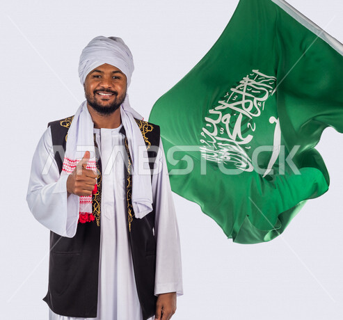 بورتريه لرجل عربي سوداني مبتسم ، خلفه علم المملكة العربية السعودية، ذكرى اليوم الوطني السعودي، الاحتفال بالعيد الوطني السعودي ، خلفية بيضاء لرجل سوداني مسلم يرتدي الزي السوداني مع العمه الملفحة