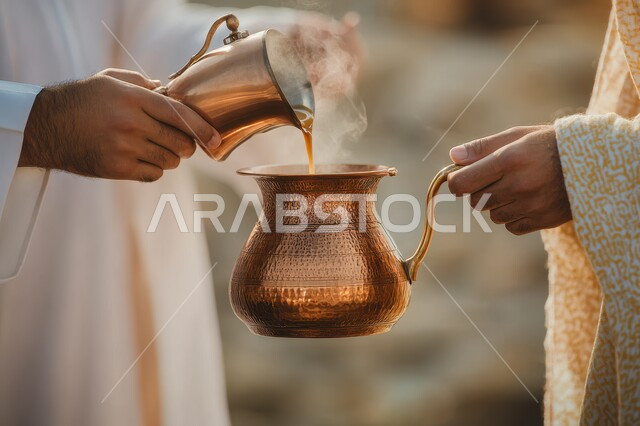 العادات والتقاليد الأصيلة, مفهوم كرم الضيافة وحسن الإستقبال، الاستمتاع بالمشروبات الساخنة، صورة مقربة لأيدي رجلين عربيين خليجيين سعوديين يرتدو الزي التقليدي يحملان  دلة قهوة عربية، التمسك بالقيم الكريمة المتوارثة من الأجداد