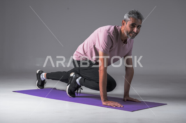 المحافظة على التوازن الجسدي، اتباع أسلوب حياة صحي، تقوية الأعصاب والعضلات، ايماءات القوة والنشاط، مفهوم اللياقة والرشاقة، بورتريه لرجل عربي خليجي سعودي يرتدي الزي الرياضي ينظرالى الكاميرا بابتسامه يقوم بممارسة التمرينات الرياضية، خلفية رمادية.