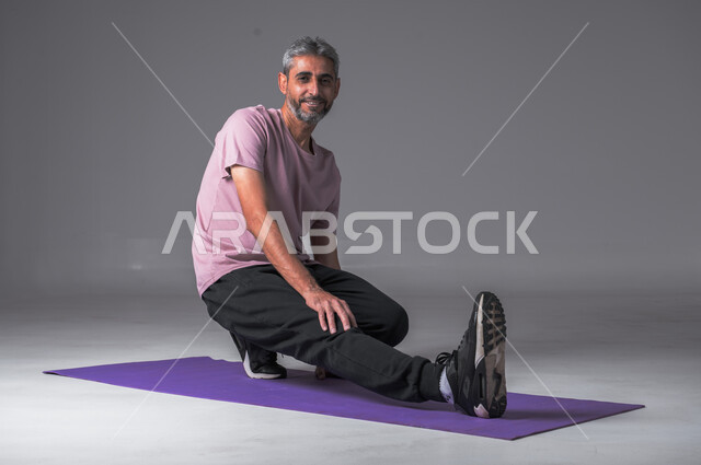   ايماءات القوة والنشاط ،المحافظة على التوازن الجسدي، اتباع أسلوب حياة صحي، تقوية الأعصاب والعضلات، مفهوم اللياقة والرشاقة، بورتريه لرجل عربي خليجي سعودي يرتدي الزي الرياضي ينظرالى الكاميرا بابتسامه يقوم بممارسة التمرينات الرياضية، خلفية رمادية.