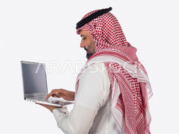 بورتريه لرجل سعودي خليجي بالزي السعودي التقليدي ، استخدام جهاز الحاسوب المحمول لإنجاز المهام والمشاريع ، خلفية بيضاء ، جلسة عمل، سيد أعمال، إنجاز المشاريع والمهام، العمل عن بعد ، مهن وأعمال تجارية ، التعليم الإلكتروني