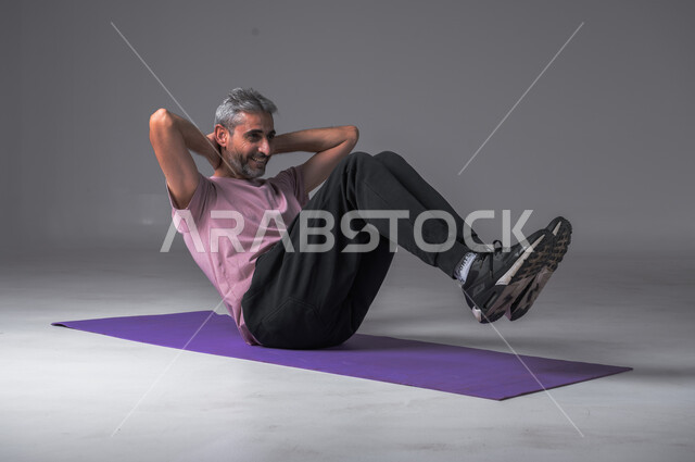 أسلوب حياة صحي ، تمدد و تسخين العضلات ،تقوية عضلات الجسم ،نشاط بدني للمحافظة على الصحة و اللياقة الجسدية ، بورتريه لرجل عربي خليجي سعودي يقوم بممارسة تمارين الإحماء الرياضية ، خلفيه رماديه