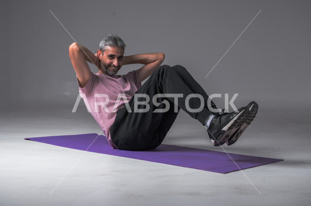 أسلوب حياة صحي ، تمدد و تسخين العضلات ،تقوية عضلات الجسم ،نشاط بدني للمحافظة على الصحة و اللياقة الجسدية ، بورتريه لرجل عربي خليجي سعودي يقوم بممارسة تمارين الإحماء الرياضية ، خلفيه رماديه