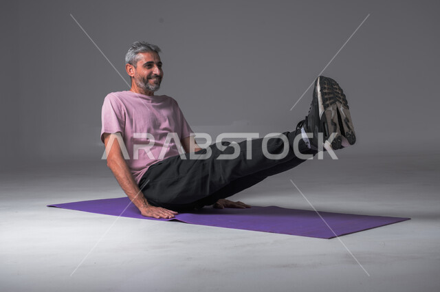  تمدد و تسخين العضلات ،تقوية عضلات الجسم ،نشاط بدني للمحافظة على الصحة و اللياقة الجسدية ، بورتريه لرجل عربي خليجي سعودي يقوم بممارسة تمارين الإحماء الرياضية ، أسلوب حياة صحي ، خلفيه رماديه