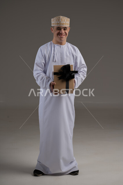 الاهتمام ودعم المجتمع العماني لذوي الاحتياجات الخاصة ، بورتريه لرجل عربي خليجي يرتدي الزي التقليدي يحمل بيده هدية, تقديم الحب و الرعاية،مفهوم طلب العون والمساعدة 