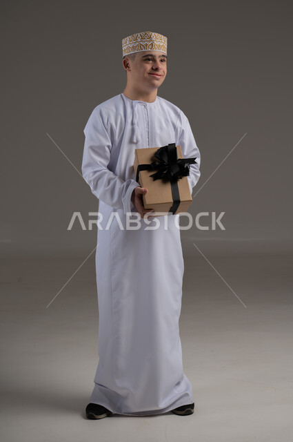 الاهتمام ودعم المجتمع العماني لذوي الاحتياجات الخاصة ، بورتريه لرجل عربي خليجي يرتدي الزي التقليدي يحمل بيده هدية, تقديم الحب و الرعاية،مفهوم طلب العون والمساعدة