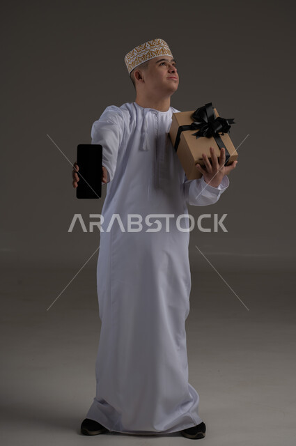 الاهتمام ودعم المجتمع العماني لذوي الاحتياجات الخاصة ، بورتريه لرجل عربي خليجي يرتدي الزي التقليدي يحمل بيده هدية, تقديم الحب و الرعاية،مفهوم طلب العون والمساعدة 