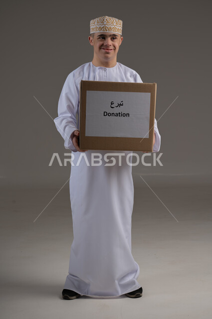 Caring and supporting the Saudi community for people with special needs, a portrait of a Gulf Arab man wearing traditional clothing holding a donation box in his hand, providing love and care, the concept of asking for help and assistance.