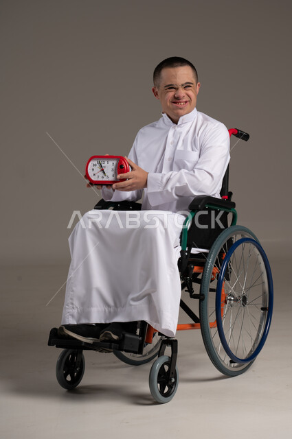Providing love, care, attention and support to the Omani community for people with special needs, a portrait of a Gulf Arab man wearing traditional clothing holding an alarm clock in his hand.