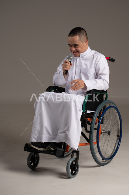إيماءات وجه ويد تدل على السعادة، بورتريه لشاب عربي سعودي خليجي يرتدي الثوب التقليدي يحمل بيده مكريفون, التمكين الاجتماعي للمعاقين, اهتمام ودعم المجتمع السعودي لذوي الاحتياجات الخاصه, تقديم الحب و الرعاية