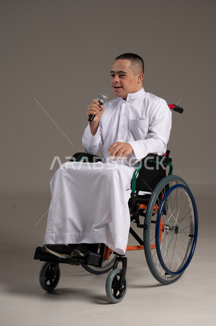 Face and hand gestures indicating happiness, portrait of a Saudi Gulf Arab young man wearing a traditional dress holding a microphone in his hand, social empowerment of the disabled, Saudi society’s interest and support for people with special needs, providing love and care