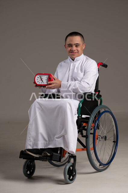 Providing love, care, attention and support to the Omani community for people with special needs, a portrait of a Gulf Arab man wearing traditional clothing holding an alarm clock in his hand.