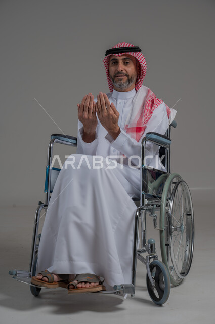 Worship and drawing closer to God, supplication to the Lord of the servants, the concept of the pillars of Islam, a portrait of a disabled Saudi Arabian Gulf man wearing traditional thobe and shemagh sitting in a wheelchair raising his hands in gestures of supplication, a full body image, gray background
