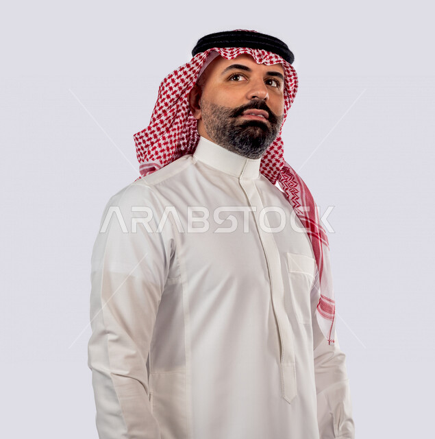 بورتريه بصورة مقربة لرجل سعودي خليجي يقوم بجلسة تصوير بإيماءات وجه ويدين مختلفة ، منظر جانبي لرجل سعودي يرتدي زي تقليدي سعودي مع شماغ وعقال ، خلفية بيضاء