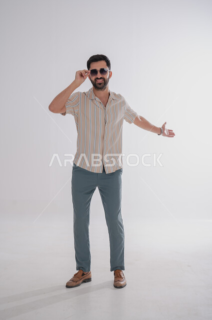 Gestures of welcoming someone, looking at the camera with an expression of pleasure, portrait of a smiling Saudi Gulf Arab man wearing sunglasses, full-length body portrait, white background