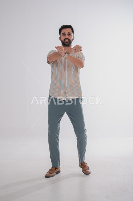 النظر إلى الكاميرا بتعابير الفرح والسرور، الوقوف بايدي متقاطعة, بورتريه لرجل عربي خليجي سعودي مبتسم، الجسم بالطول الكامل, خلفية بيضاء