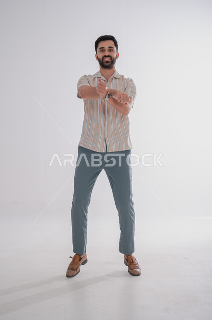 النظر إلى الكاميرا بتعابير الفرح والسرور، الوقوف بايدي متقاطعة, بورتريه لرجل عربي خليجي سعودي مبتسم، الجسم بالطول الكامل, خلفية بيضاء