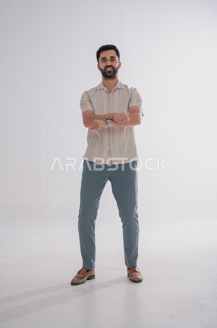 النظر إلى الكاميرا بتعابير الفرح والسرور، الوقوف بايدي متقاطعة, بورتريه لرجل عربي خليجي سعودي مبتسم، الجسم بالطول الكامل, خلفية بيضاء