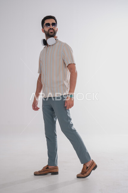 الإستماع للأغاني باستخدام الهيدفون، بورتريه لرجل عربي خليجي سعودي يرتدي النظارة الشمسية ويضع سماعات الراس حول رقبته، الجسم بالطول الكامل, خلفية بيضاء