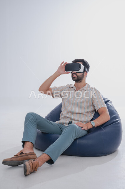 Gestures of integration and interaction with the imaginary world, portrait of a Saudi Gulf Arab man wearing 3D VR glasses, virtual reality simulation using advanced modern technologies, white background