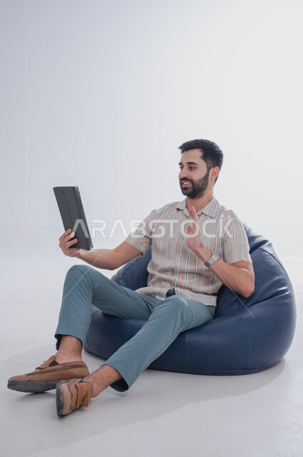 مفهوم التواصل مع العائلة بواسطة برامج التواصل الاجتماعي, بورتريه لرجل عربي خليجي سعودي يحمل بيده جهاز تابليت, ايماءات التحدث مع الاصدقاء باستخدام التقنيات المتطورة والحديثة, خلفية بيضاء