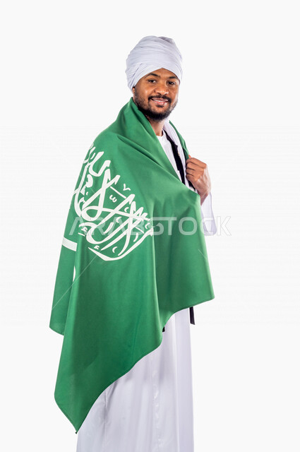 بورتريه لرجل عربي سوداني مبتسم يضع على ظهره علم المملكة العربية السعودية، ذكرى اليوم الوطني السعودي، الاحتفال بالعيد الوطني السعودي ،خلفية بيضاء لرجل سوداني مسلم يرتدي الزي السوداني مع العمه الملفحة