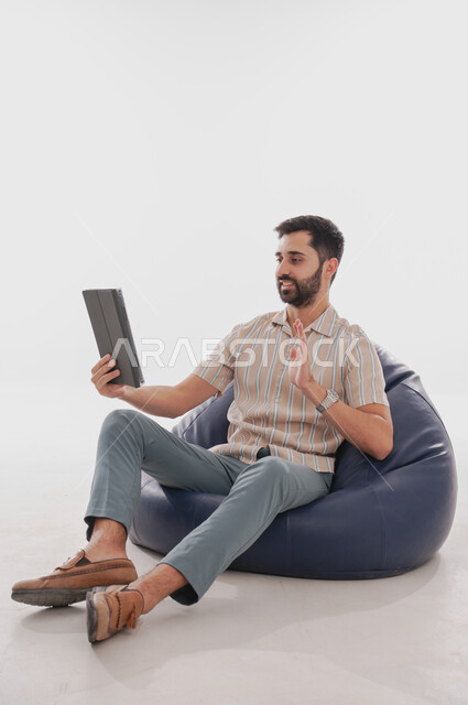 مفهوم التواصل مع العائلة بواسطة برامج التواصل الاجتماعي, بورتريه لرجل عربي خليجي سعودي يحمل بيده جهاز تابليت, ايماءات التحدث مع الاصدقاء باستخدام التقنيات المتطورة والحديثة, خلفية بيضاء