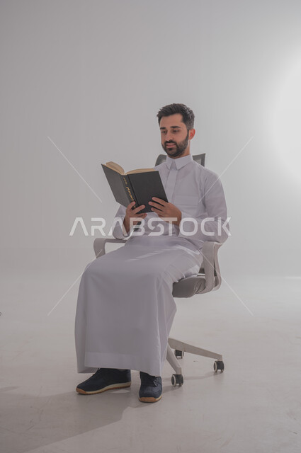إنجاز الواجبات اليومية, قضاء الوقت بالمطالعة والتعلم والتثقف, بورتريه لرجل عربي خليجي سعودي يحمل بيده كتاب للقراءة, خلفية بيضاء