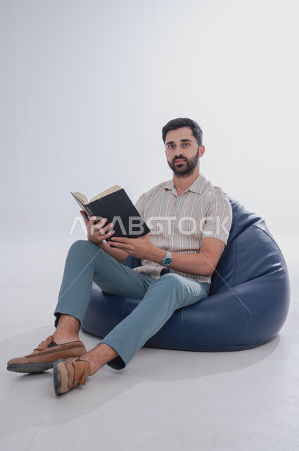 Completing daily duties, spending time reading, learning and acculturating, portrait of a Saudi Gulf Arab man holding a reading book in his hand, white background