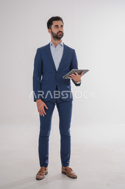 استخدام الأجهزة التقنية الحديثة, بورتريه لرجل عربي خليجي سعودي يرتدي  البدلة الرسمية ويحمل بيده التابليت، الدردشة مع الأهل والأصدقاء, تصفح برامج التواصل الاجتماعي، تطبيقات الأجهزة اللوحية، صورة الجسم بالطول الكامل, خلفية بيضاء