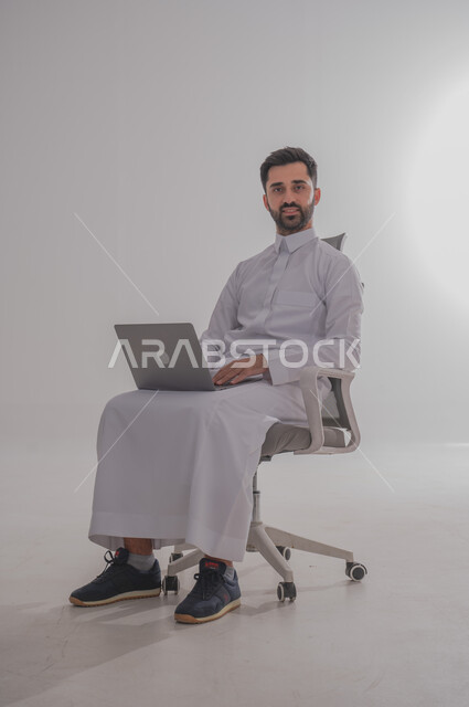 استخدام الأجهزة التقنية الحديثة, بورتريه لرجل عربي خليجي سعودي يرتدي  الثوب ويجلس على كرسي ويضع امامه حاسب محمول، الدردشة مع الأهل والأصدقاء, تصفح برامج التواصل الاجتماعي، تطبيقات الأجهزة الحاسوبية،  خلفية بيضاء