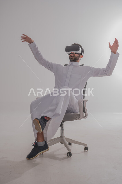 إيماءات الاندماج والتفاعل مع العالم الخيالي، بورتريه  لرجل عربي خليجي سعودي يرتدي الثوب يجلس ويضع نظارة الفي آر ثلاثية الأبعاد، محاكاة الواقع الافتراضي باستخدام التقنيات الحديثة المتطورة، خلفية بيضاء